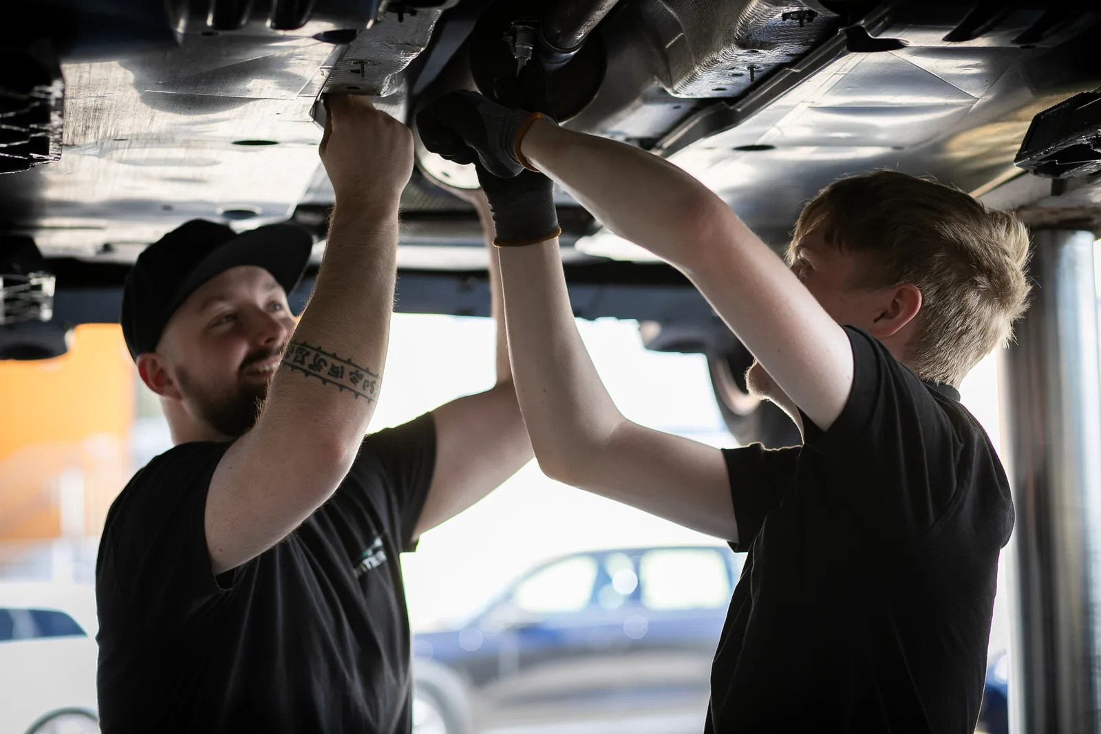 Zwei Kollegen arbeiten gemeinsam unter einem Fahrzeug